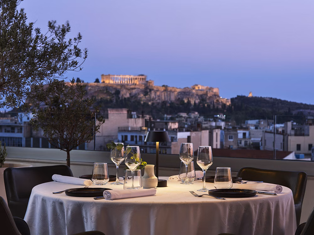 Rooftop restaurant table at Titania Hotel with the Acropolis lit at dusk